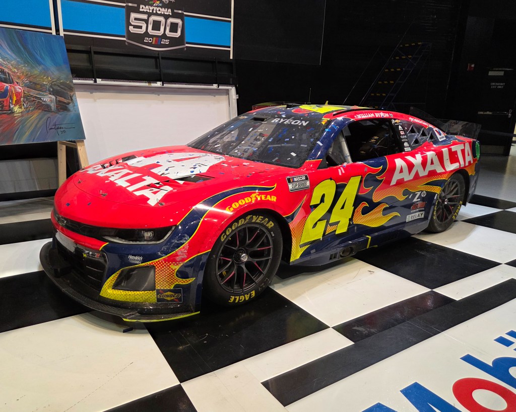 Red and black Hendrick Motorsports NASCAR race car number 24 with Axalta livery, parked on a black-and-white checkered floor.