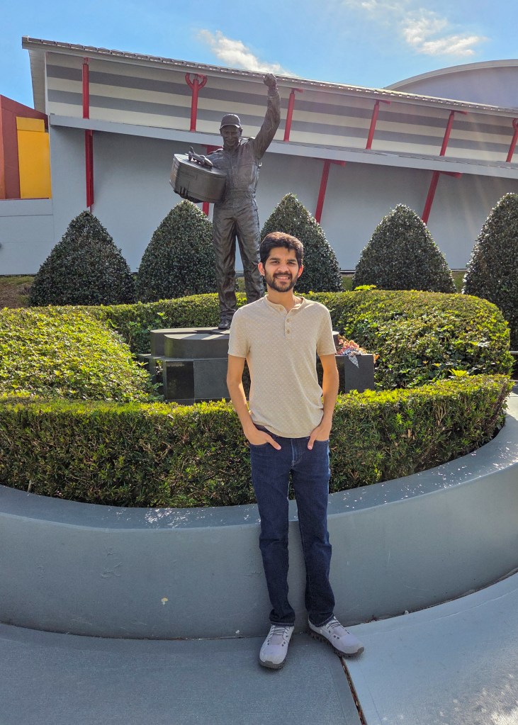 Bronze statue of Dale Earnhardt Sr. standing outdoors with hands in pockets, surrounded by manicured green hedges at the NASCAR Hall of Fame